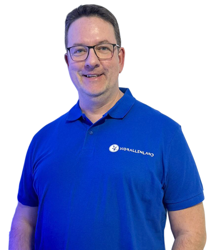 Gerd Raabe in blauem Polo-Shirt lächelt, vor einem weißen Hintergrund.